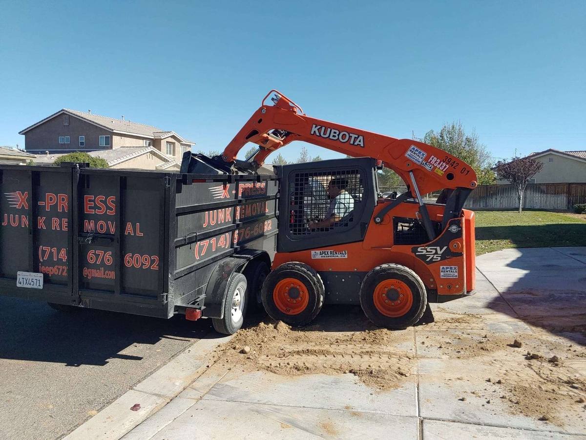 X-Press branded dump trailer and skid steer at a High Desert job site